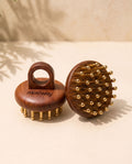 Two wooden Kansa scalp massagers with copper massage tips, one showing the handle side engraved with 'maiéway' and the other showing the brush head, set on a beige surface with soft shadows.