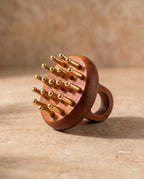 A Kansa scalp massager with copper massage pis, resting on a textured beige stone surface against a matching beige background.