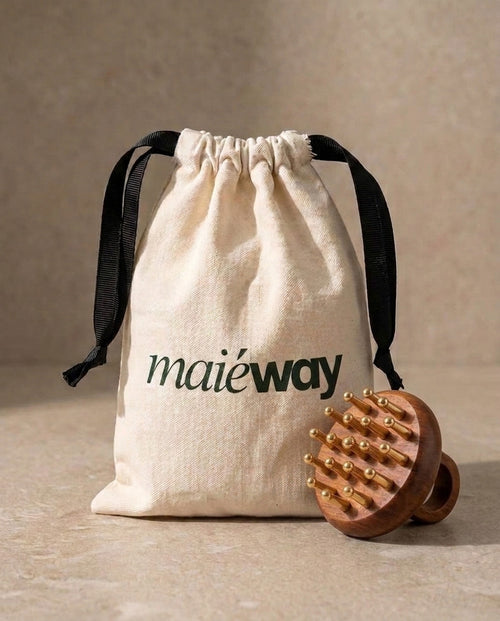 A beige drawstring pouch with black ribbon ties and the printed brand name 'maiéway' in dark green, shown next to a Kansa rosewood scalp massage tool with copper massage pins on a beige stone-like surface.