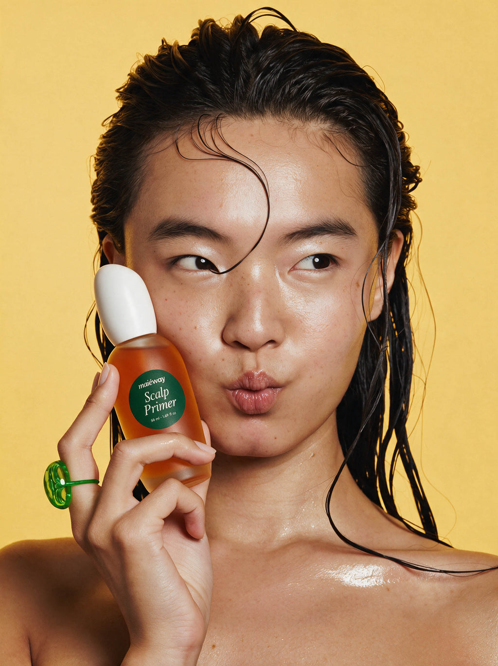 A close-up lifestyle shot of a model with wet hair holding a bottle of Scalp Prime 5 Scalp Primer against a solid yellow background.