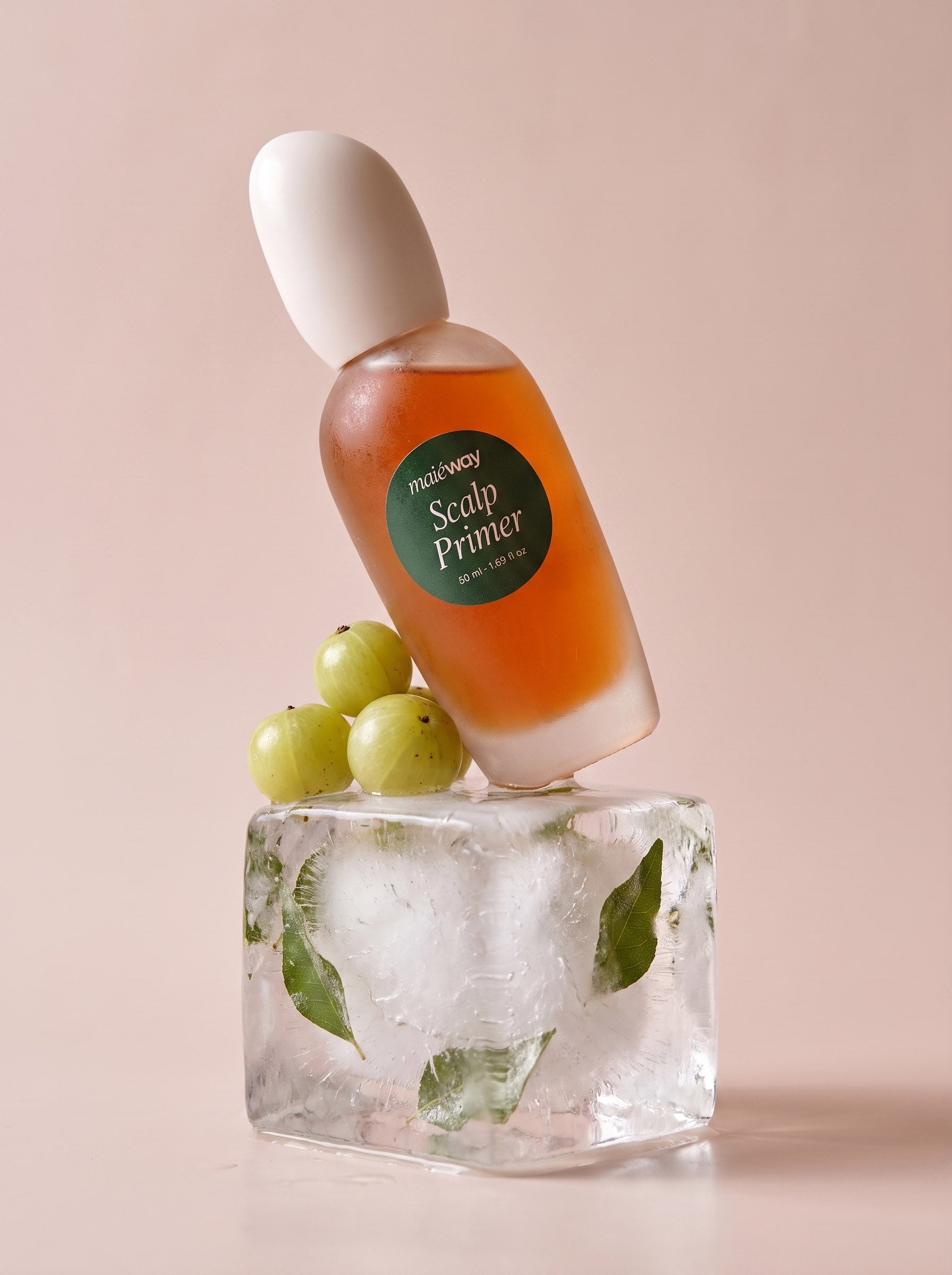 A bottle of Maieway Scalp Primer with amber liquid and a white cap, displayed on a clear ice cube with curry leaves and three goosberries against a soft pink background.