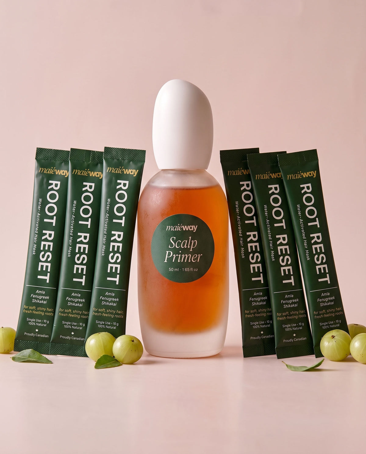 A bottle of Maieway Scalp Primer bundled with Root Reset variant flanked by six packets of the Root Reset hair mask on a soft pink background with green gooseberries as props.